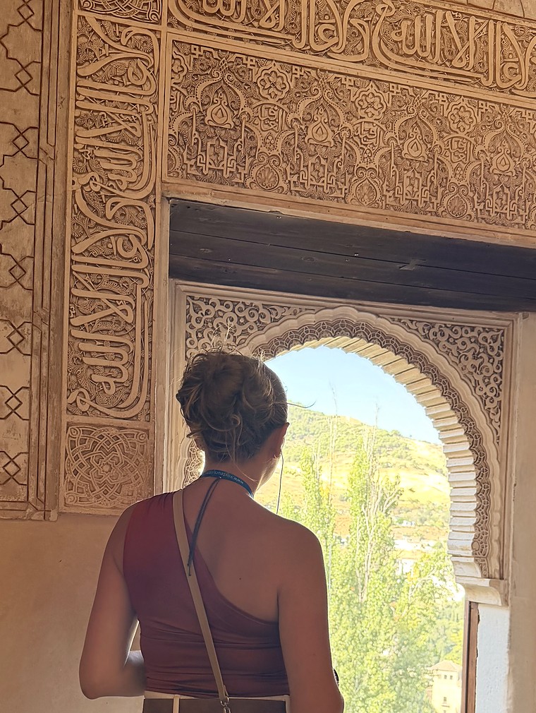 Hala Hijazi en la Alhambra, mirando por una ventana en arco.